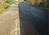 Zdjęcie przedstawia asfaltową drogę z chodnikiem po lewej stronie.
