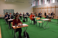 Radni powiatu płońskiego i zaproszeni goście siedzą pojedynczo przy stolikach podczas obrad sesji