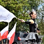Mażoretka w trakcie występu z flagą. W tle polskie flagi.