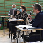 Wicestarosta Krzysztof Wrzesiński przemawia do mikrofonu siedząc w ławce, w tle starosta Elżbieta Wiśniewska i pracownik starostwa