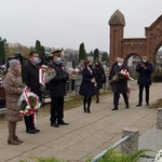 Przedstawiciele powiatu płońskiego i urzędu miasta z kwiatami na cmentarzu stoją przed mogiłą poległych żołnierzy.jpg