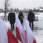 Starosta Płoński z kwiatami w rękach wraz z Wicestarostą i Przewodniczącym Rady Powiatu stoją na ośnieżonej ziemi na pierwszym planie flagi biało-czerwone