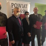 Przedstawiciele jednostek strzeleckich wraz ze Starostą i Przewodniczącym Rady stoją na tle rollupu powiatu płońskiego