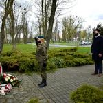 Członek Zarządu stoi przed pomnikiem w Raciążu po złożeniu kwiatów, przy pomniku stoi obsługa mundurowa