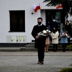 Członek Zarządu Powiatu Płońskiego Artur Adamski idzie z wiązanką kwiatów w tle inni uczestnicy uroczystości zorganizowanej w Raciążu