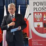Przewodniczący Rady Powiatu Płońskiego przemawia stojąc, w tle rollup z herbem powiatu
